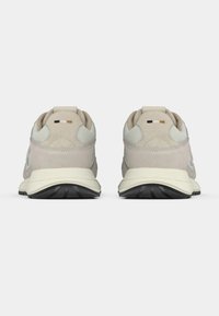 Bézs sportcipő mintás felsőrésszel, hálós oldalsó részletekkel és fehér középtalppal. Húzófüllel és fekete gumitalppal rendelkezik.