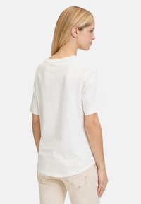 Hvid bomulds t-shirt med korte ærmer, rund halsudskæring og en let buet kant. Glat tekstur, minimalistisk design, ingen synlige mønstre.