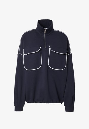 Marineblauwe pullover met hoge kraag en ritssluiting. Voorzien van witte piping langs de schouders en twee grote zakken aan de voorkant. Zachte textuur.