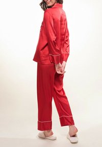 Ensemble de pyjama en satin rouge avec des manches longues et des accents blancs en passepoil. Haut et pantalon ample, en tissu doux et texturé.