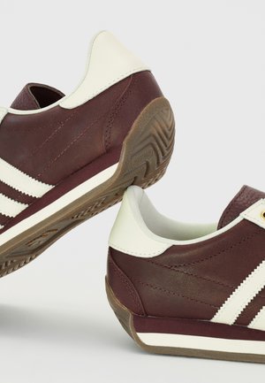 Brązowo-białe sneakersy w stylu retro z teksturowaną gumową podeszwą i białymi paskami po bokach.