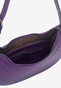 Fialová kožená kabelka na rameno s hladkou textúrou, zapínaním na zips a hnedým textilným vnútrom. Má vnútornú kapsu s vyrazeným logom.