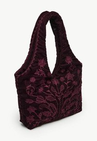 Geborduurd fluwelen tasje in diep bordeauxrood met bloemmotieven en een gestructureerd oppervlak. Voorzien van twee brede, zachte schouderbanden.