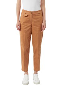 Pantaloni di cotone beige con una vestibilità comoda, caratterizzati da chiusura con bottone anteriore, tasche laterali e gamba tapered. Indossati con sneakers bianche.