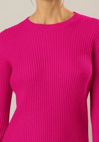 Maglione attillato a coste in fucsia vivace. Presenta un collo rotondo e maniche lunghe, che mettono in mostra un motivo di maglia testurizzato.