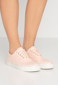 Světlé růžové plátěné tenisky s nízkým profilem, kulatou špičkou, kovovými očka a bílou gumovou podrážkou se subtilním pruhovaným vzorem.