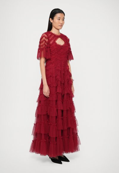 Raudona sluoksniuota suknelė, pagaminta iš tiulio. Savybės: trumpi rankoviai, rakto skylutės iškirptė ir sluoksniuoti volai visame audinyje. Dėvima su juodais batais.