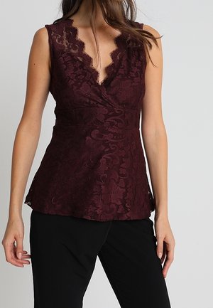 Bordowa koronkowa bluzka z marszczonym dekoltem i bez rękawów. Posiada kwiatowy wzór i teksturowaną tkaninę, zestawiona z czarnymi spodniami.