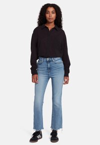 Maglietta nera a maniche lunghe con chiusura a bottoni, abbinata a jeans azzurri a vita alta con orlo sfilacciato. Sneakers nere completano l'outfit.