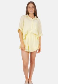 Ensemble en coton jaune, léger et texturé, comprenant une chemise à manches courtes à boutons et un short assorti avec un ourlet à volants.