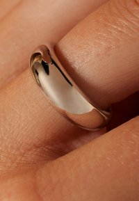 Polierter Metallring an einem Finger, mit einem glatten, abgerundeten Design. Die Oberfläche reflektiert Licht und verstärkt das elegante Aussehen.