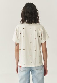 Witte short-sleeve shirt met gevarieerde kleurrijke borduursels van bloemen en insecten, met een ontspannen pasvorm en opgerolde mouwen.