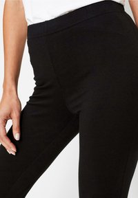 Leggings neri con vita elasticizzata, caratterizzati da una superficie liscia e una silhouette aderente. Nessuna cucitura o motivo visibile.