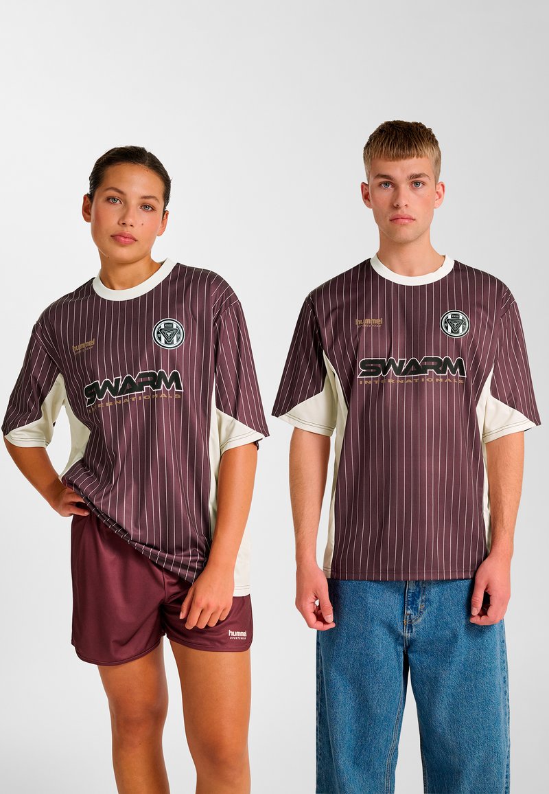 Stribede sports T-shirts i bordeaux og creme med korte ærmer, der har logo og teksten 'SWARM'. Matchende bordeaux shorts og blå denimjeans.