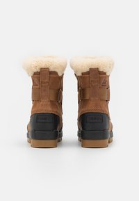Botas de invierno de cuero marrón con un forro esponjoso de color crema, suelas de goma negra y correas ajustables a los lados.