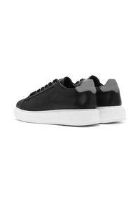 Sneaker in pelle nera con finitura liscia, suola in gomma bianca, dettagli in grigio sul tallone e pannello laterale perforato. Presentano lacci tondi.