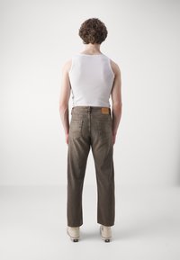 Brune denim jeans med rett ben-snitt, baklommer, og en lys lær-lapp på midjebåndet. Brukt med en hvit ermeløs topp.