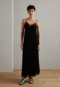 Svart maxiklänning med spetsdetaljer, tunna axelband och en luftig silhuett. Matchad med gröna sandaler med justerbara remmar och platt sula.