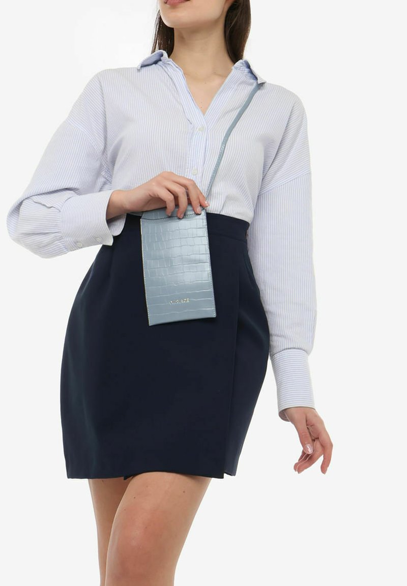 Lyseblå stribet skjorte med knapstolpe, marineblå nederdel og en struktureret lyseblå crossbody taske med krokodillemønster.