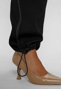 Joggers noirs texturés avec surpiqûres blanches, ajustables à la cheville, associés à des chaussures à talons hauts nude brillantes avec une base carrée.