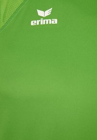 Tissu de sport vert avec un logo blanc de la marque Erima et un emblème en forme d'aile près de l'encolure.