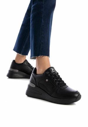 Baskets noires avec une tige texturée, fermeture à lacets et une semelle épaisse et surélevée. Les caractéristiques incluent des accents subtils et un design à bout arrondi.
