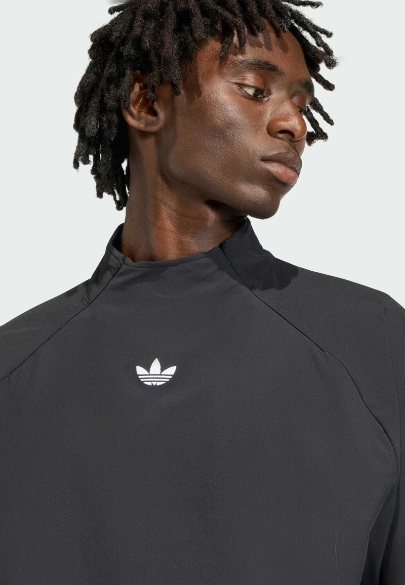 Schwarze Sportjacke mit hohem Kragen und weißem Adidas-Logo auf der Brust, gefertigt aus einem glatten, leichten Material und mit einem eleganten Design.