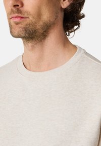 Light beige sweatshirt with a soft texture, crew neckline, and ribbed accents at the collar. Close-up view features minimal stitching details.