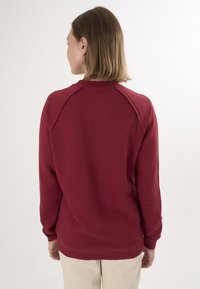 Bordowy sweatshirt uszyty z miękkiej tkaniny, z rękawami raglanowymi i okrągłym dekoltem. Widok z tyłu ukazuje czysty, prosty design bez ozdób.
