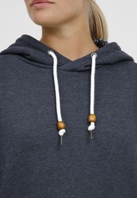 Le sweat à capuche gris charbon est doté d'un cordon de serrage avec des perles en bois, des embouts en métal argenté et une doublure intérieure à motifs. Texture de tissu douce.