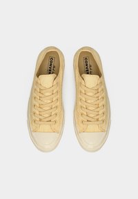 Baskets en toile jaune avec une finition texturée, dotées de lacets assortis, d'une semelle en caoutchouc et d'un bout rond. Marquage minimal visible à l'intérieur.