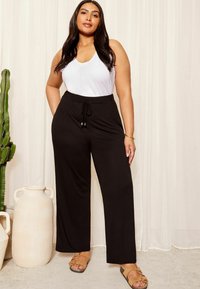 Pantalones anchos negros con cintura ajustable, combinados con una camiseta sin mangas blanca. Presenta una textura suave y sutiles acentos metálicos en el cordón.