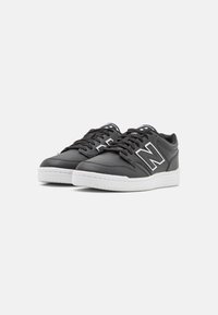 Svarta lädersneakers med vit gummisula och snörning, med en perforerad design och en framträdande vit logga på sidan.