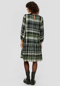 Karo-Kleid in Grün, Schwarz und Creme mit gestuftem Saum, langen Ärmeln und einem Schlüsselloch-Ausschnitt hinten. Aus weichem Stoff gefertigt. Schwarze Knöchelschuh.