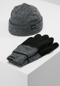 Knitted gray beanie with textured pattern, and black gloves with gray accents. Both feature a brand label.