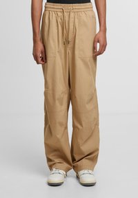 Beige cargo pants with an elastic waistband, adjustable drawstring, two side pockets, and a relaxed fit, paired with white sneakers.