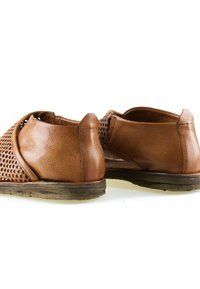 Chaussures décontractées en cuir marron avec des côtés perforés et des semelles en caoutchouc usées, vues de dos sur un fond blanc.