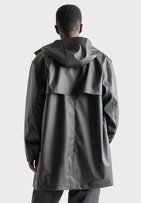 Lang, mørkegrå regnfrakke lavet af vandafvisende materiale med hætte, rygventilation og sidelommer, med et minimalistisk design.