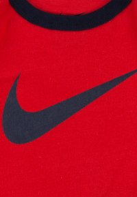 Rød bomull T-skjorte med et stort svart Nike-logo. Rund svart ribbestrikket hals, myk tekstur og korte ermer.