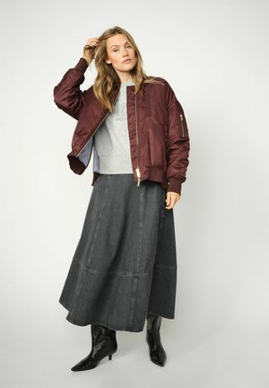 Burgundy bomber jacket with ribbed collar, grey sweatshirt, and long dark denim skirt. Black pointed toe boots with a glossy finish.