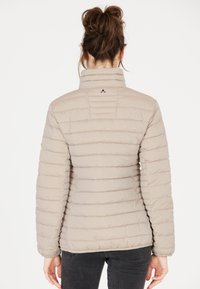 Beige pufferjacka med horisontell sömnad, hög krage och diskret logo på baksidan. Strukturerad tyg och slim fit-design.