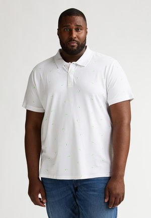 Witte poloshirt met verspreide groene bladpatronen, korte mouwen en een kraag, gecombineerd met donkerblauwe spijkerbroek.