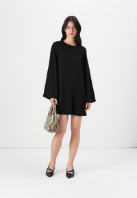 Vestido negro de manga larga con escote redondo. Combinado con un bolso de textura de serpiente y zapatos negros de punta. Diseño sencillo, con detalles mínimos.