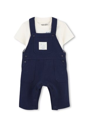 Marineblauwe baby-overall met voorzakken en drukknopen gecombineerd met een wit T-shirt met korte mouwen en een kleine print aan de binnenkant van de kraag.