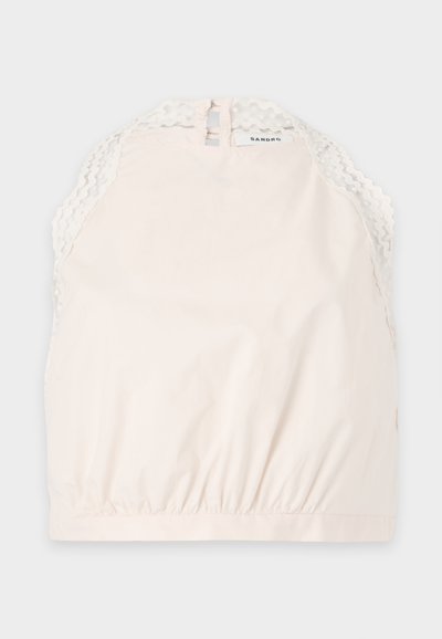 Haut sans manches crème avec bordure en dentelle à volants sur les épaules et col montant, bande élastique en bas, petite fermeture à bouton au dos.