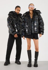 Black glossy puffer jackets with oversized hoods, featuring quilted sections. Model pairs with a black mini skirt and knee-high platform boots.