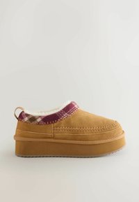 Tan suède instappers met een paarse ruitaccent, witte fluffy voering, contrasterende stiksels en een gestructureerde rubberen zool.