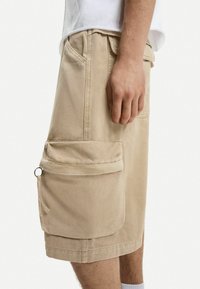 Beige cargo shorts i bomuldsstof med sidelommer, featuring en flap og metalhardware detaljer, knæ-længde med en afslappet pasform.
