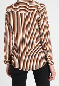 Chemise à boutons rayée avec des rayures verticales marron et blanches, manches longues, ourlet arrondi et poignets à un seul bouton. Texture de tissu lisse.