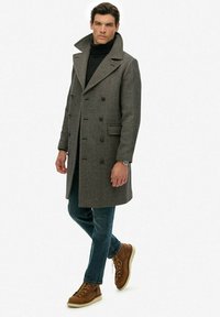Grijze wollen peacoat met grote revers en dubbelgeknoopte knopen, gecombineerd met donkere jeans en bruine veterschoenen. Glad textuur door het geheel.